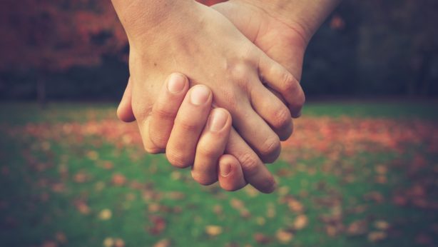 Close up on a couple holding hands in the park in autumn