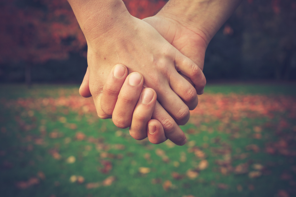 Close up on a couple holding hands in the park in autumn